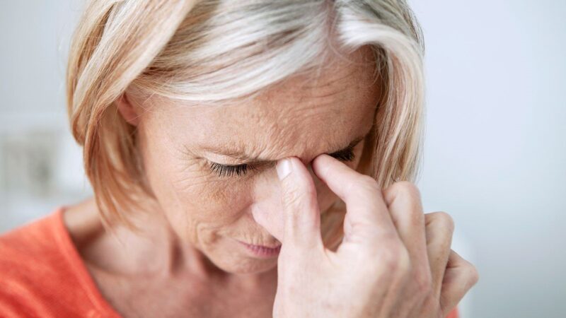 Woman pressing fingers to nose experiencing sinus pain and headache
